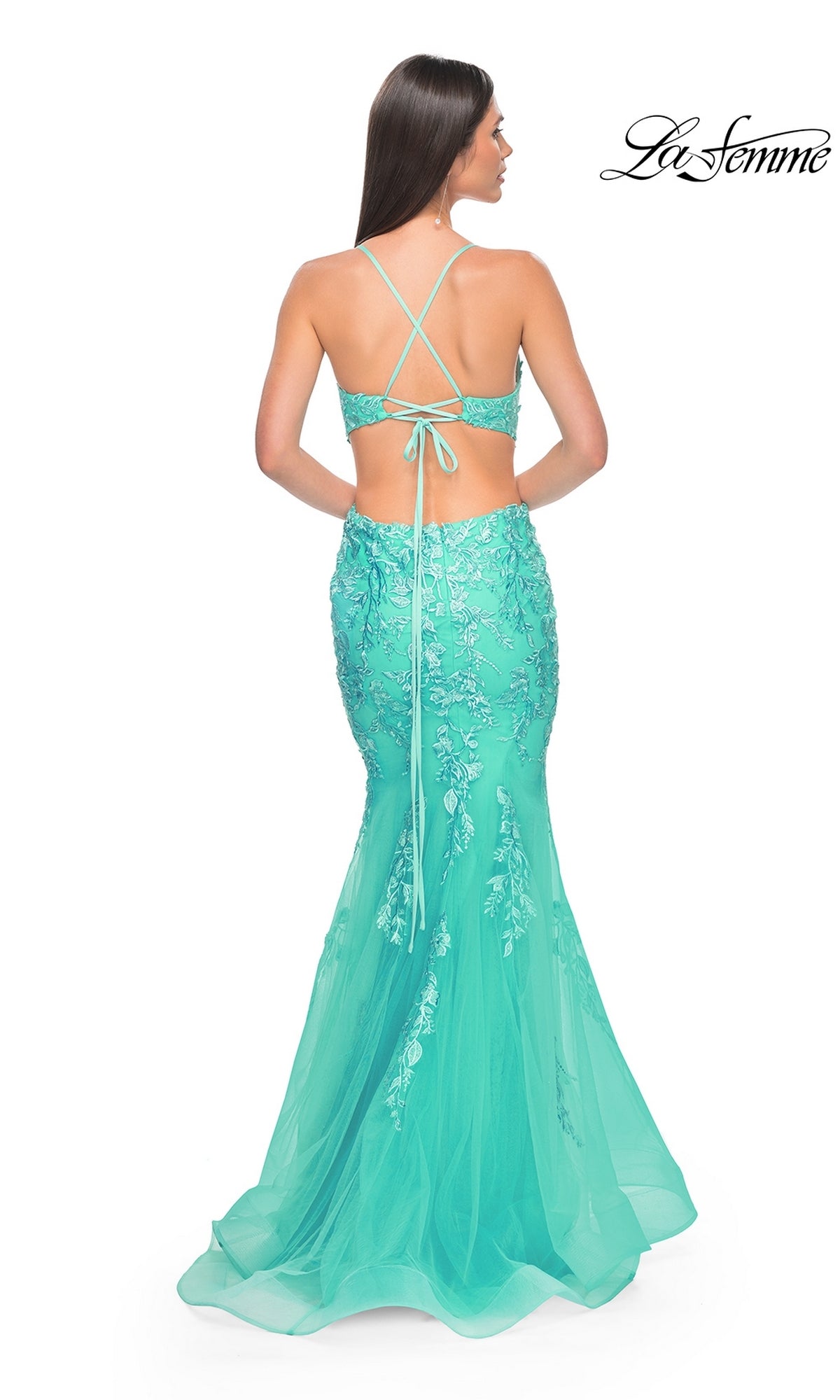 Woman wearing the La Femme Long Lace Mermaid Prom Dress 31133 in turquoise, featuring floral embroidery and a crisscross corset back, stands facing away.